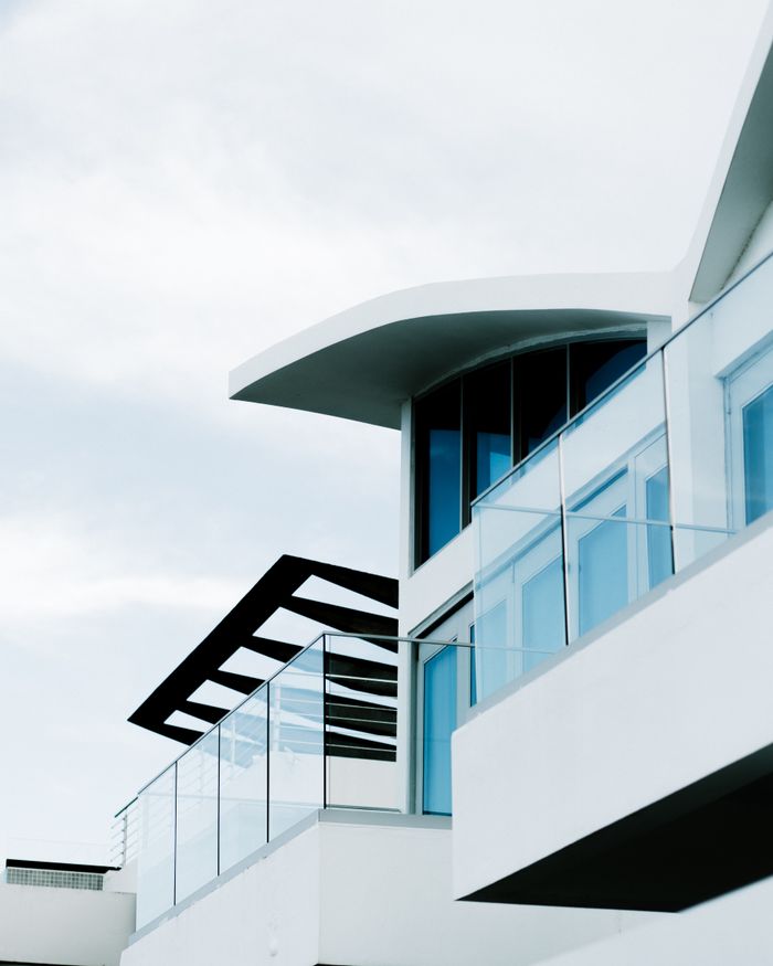 Low angle view of a modern building featuring glass balconies against a cloudy sky.